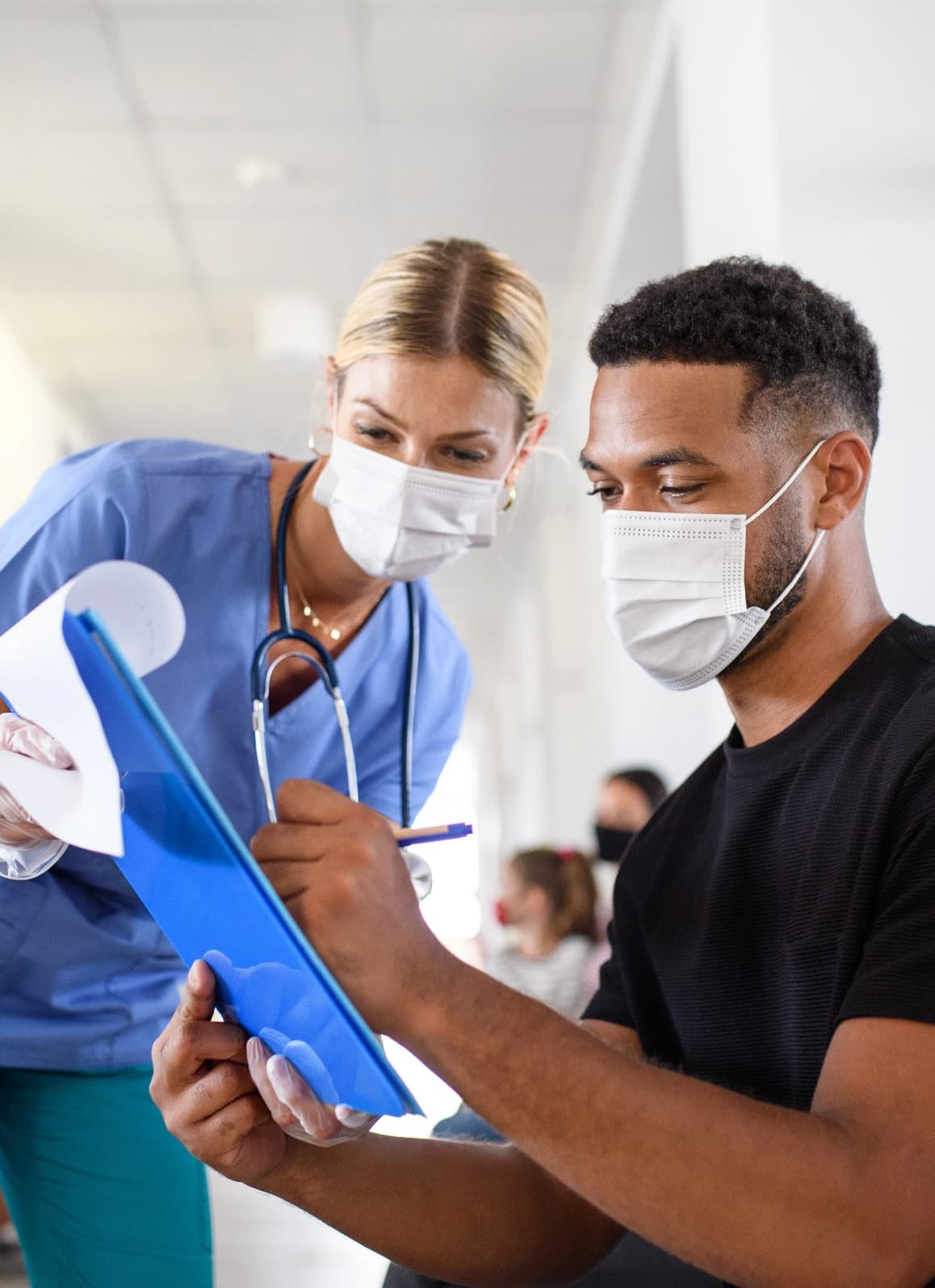 Patient signing clipboard with nurse looking on