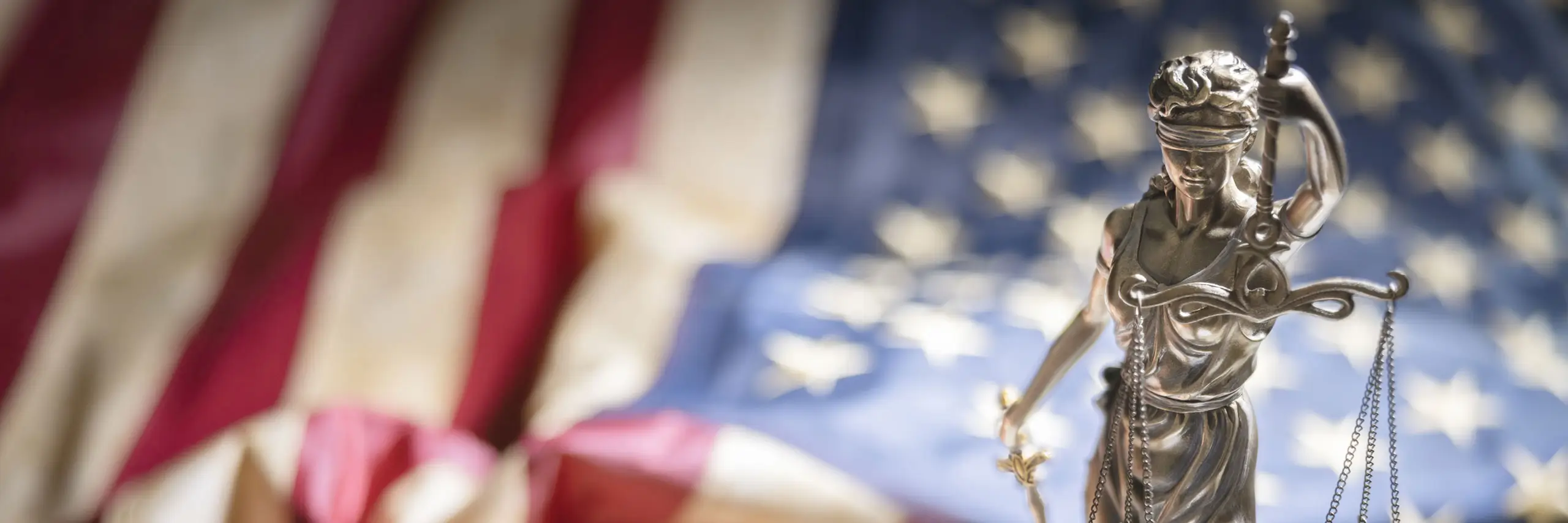 Statue of Lady Justice with scales in front of a blurred American flag, symbolizing justice, law, legal compliance, and the U.S. legal system.