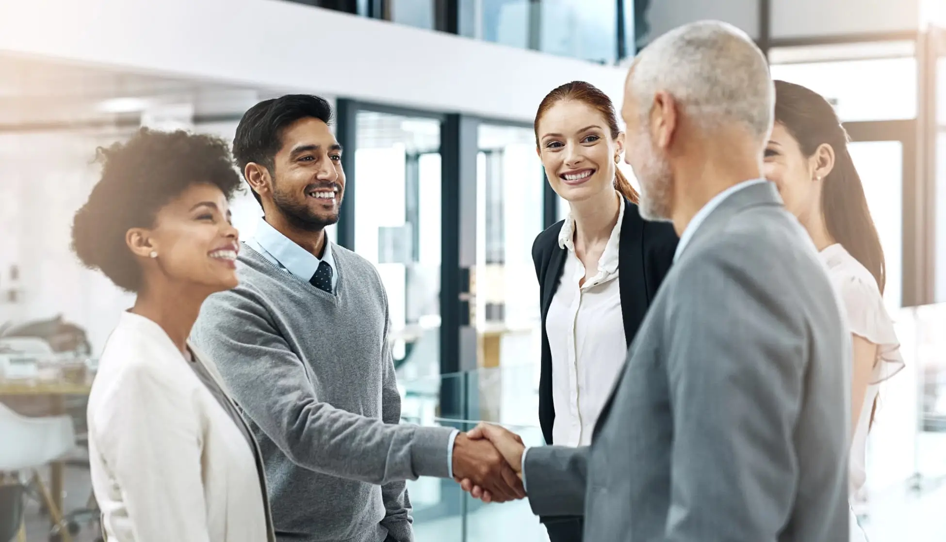 A diverse group of business professionals smiling and shaking hands during a meeting in a modern office, symbolizing teamwork, partnership, and collaboration.