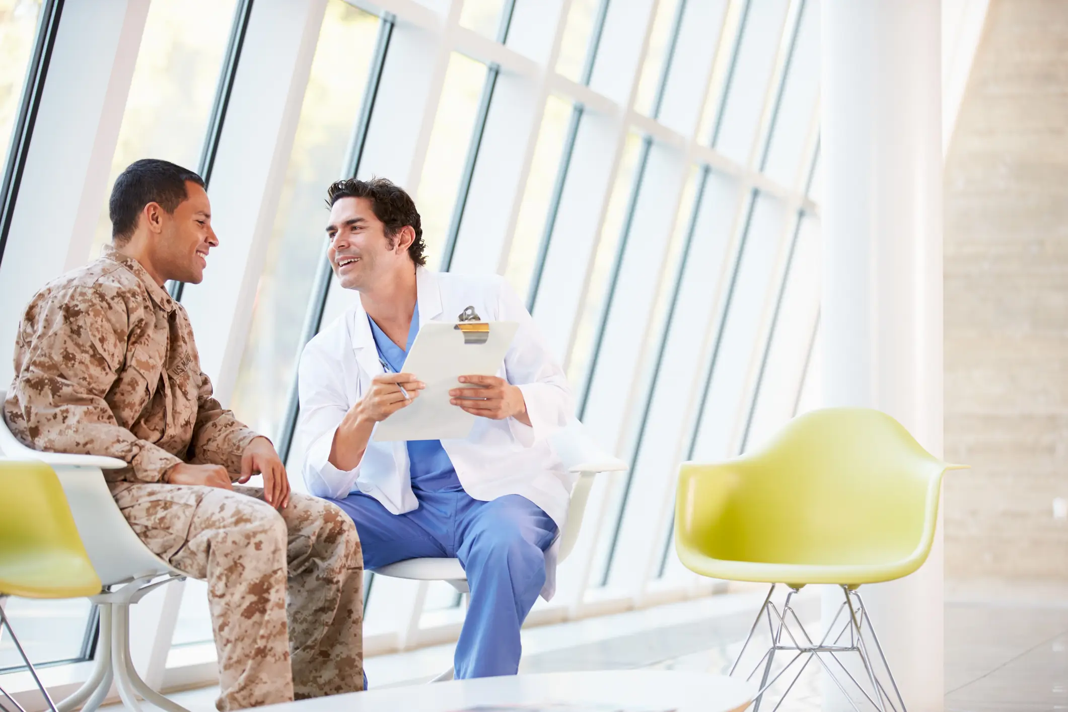 A healthcare professional consulting with a military service member in a medical facility, reviewing health information and discussing treatment options.