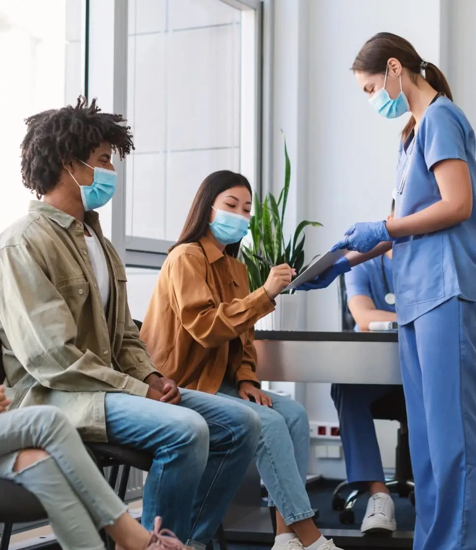 Nurse assisting masked patients with clinic registration in a clean and modern medical waiting room.